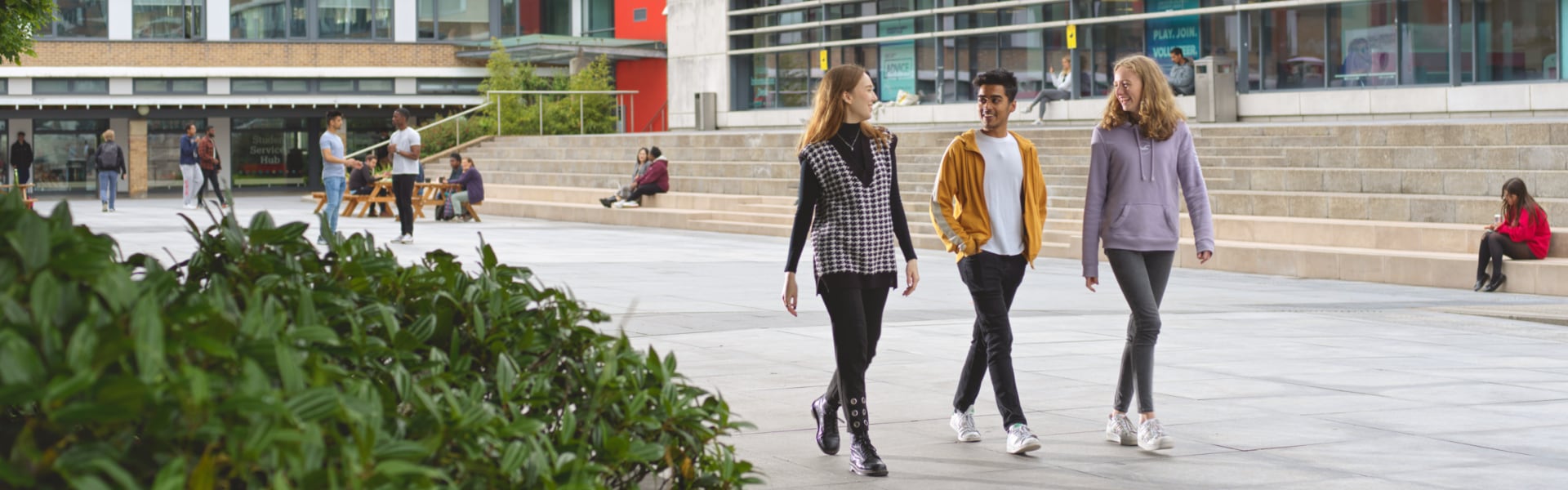 Three smiling students walk across Alexandra Square